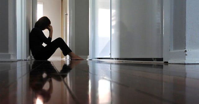 A stressed woman wearing black shirt and pants sitting barefooted on the floor with her hand on her ...