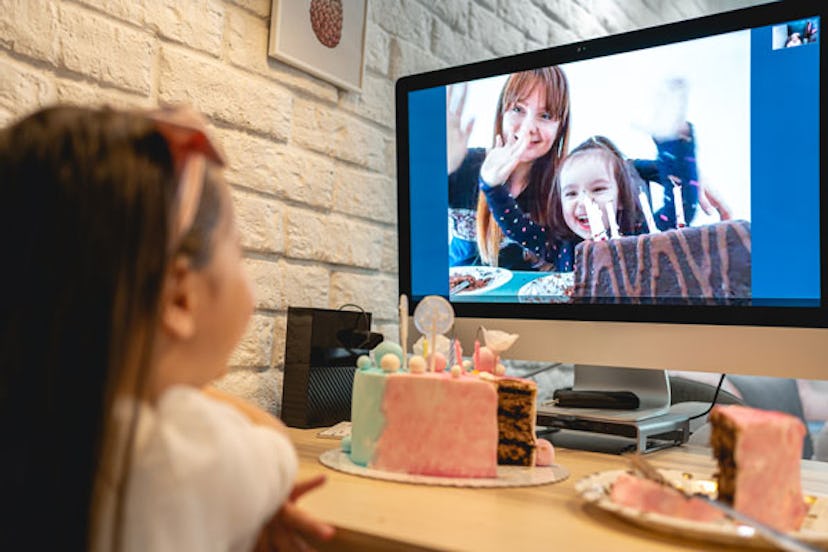 A little girl with a birthday cake in front of her looking at a TV screen