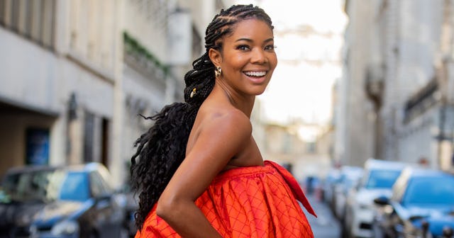 Gabrielle Union smiling in an orange sleeveless dress and walking