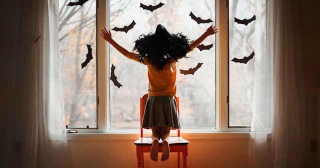 Girl in front of window decorated with bats — bat puns and jokes.