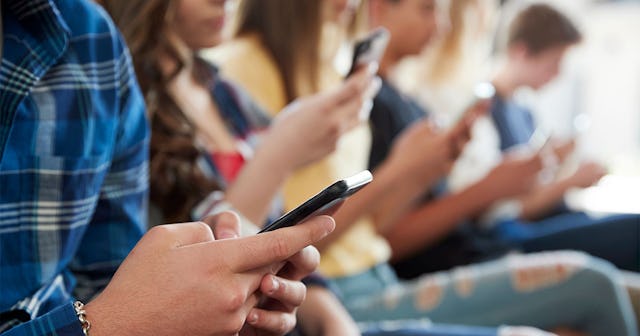A group of kids sitting in a row, all holding their phones and watching TikTok