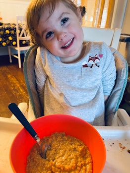 Little blonde girl smiling at the camera while her meal is standing in front of her in the orange bo...