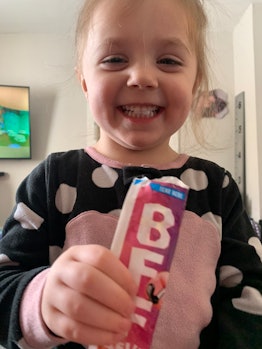 Little girl with blonde hair smiling at the camera while holding an ice cream in her hands 