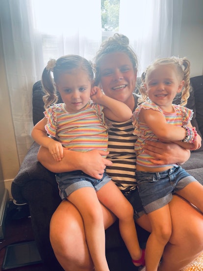 Mother holding her two blonde girls in her arms while smiling and sitting on a black couch