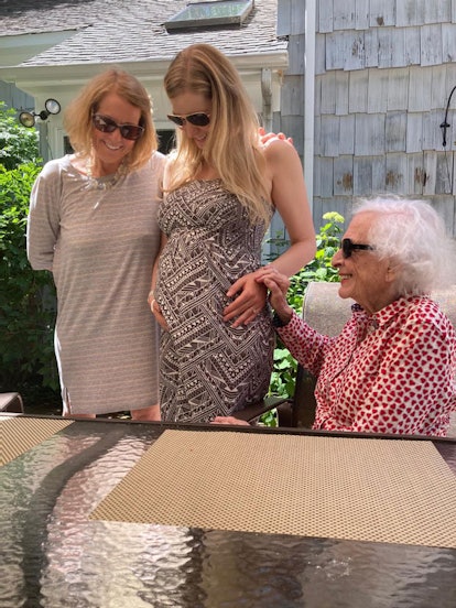 Grandmother, mom, and pregnant daughter smiling while grandmother gives granddaughter advice on chil...