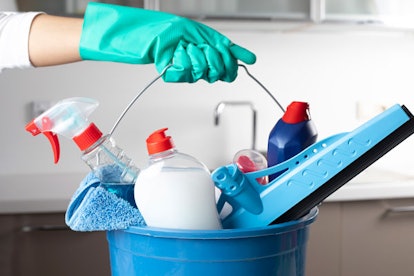 A woman's hand with a green rubber glove holding a blue bucket with cleaning supplies in it
