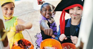 Three kids in Halloween costumes trick-or-treating and smiling