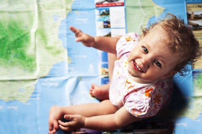 A little curly-haired girl in a white-pink-orange patterned T-shirt sitting on a world map, looking ...