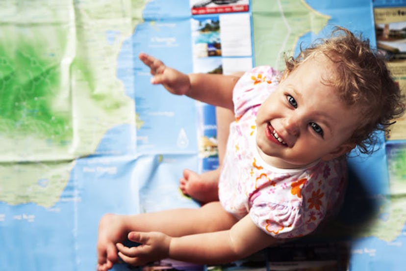 A little curly-haired girl in a white-pink-orange patterned T-shirt sitting on a world map, looking ...