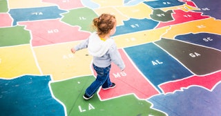A girl in a grey hoodie and denim jeans walking on the floor depicting a map of the states in Americ...