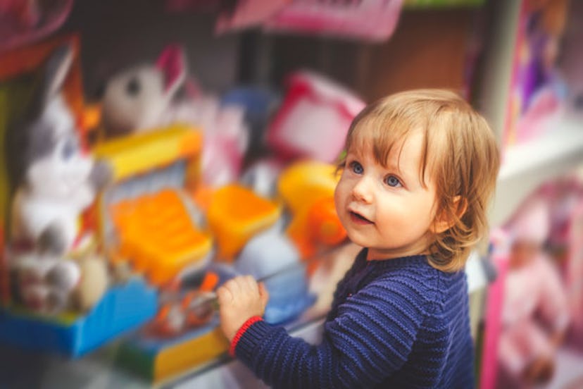A child in the navy blue sweater stands near the shelf with the toys that are blurred