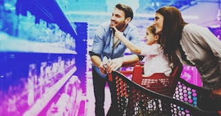 A couple and their daughter in the shopping cart pointing at toys on the shelf