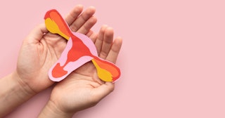 A pink-red-orange paper cutout of a uterus placed on a person's palms