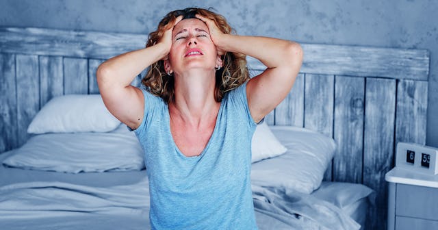 Woman sitting on the bed and pulling her hair while facing the ceiling because she can’t sleep in he...