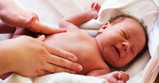 A person massaging the belly of a crying baby with newborn gut deficiency