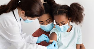 A mother holding her daughter while a doctor is putting a plaster on her arm after giving her a Covi...