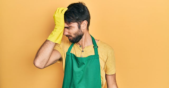 A man wearing a green apron while he's holding his head with one hand in a yellow glow.