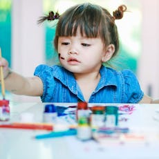 A little girl paints pictures at a table.