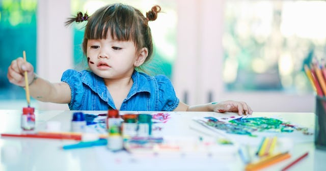 A little girl paints pictures at a table.