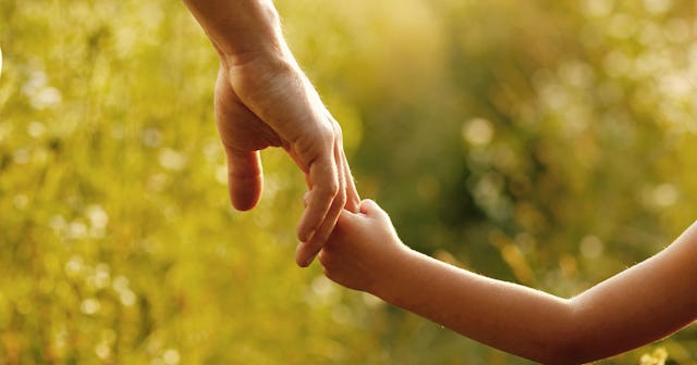 An image of a child's hand holding a parent's hand out in a grass field.