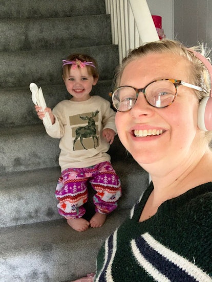 A toddler sitting on the stairs and its mother taking a selfie while they both are smiling.