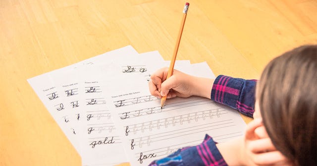 A kid writing on a cursive writing practice sheet on a wooden floor