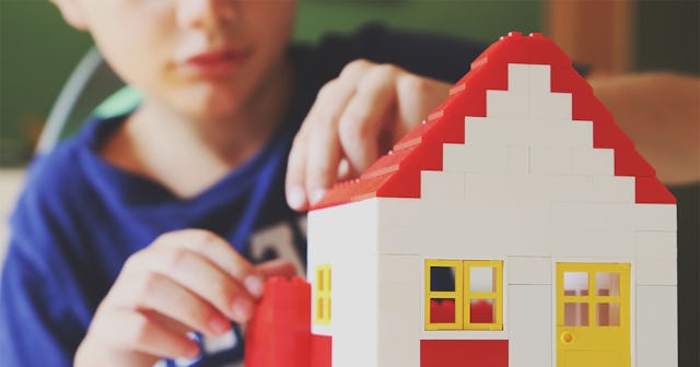 A 6-year-old boy in a blue T-shirt constructing a white house from building blocks to nurture his me...