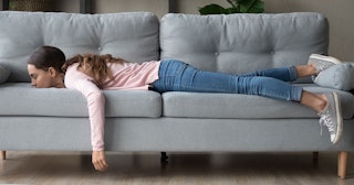 A woman in a pink top and blue denim jeans lying face down on a grey couch