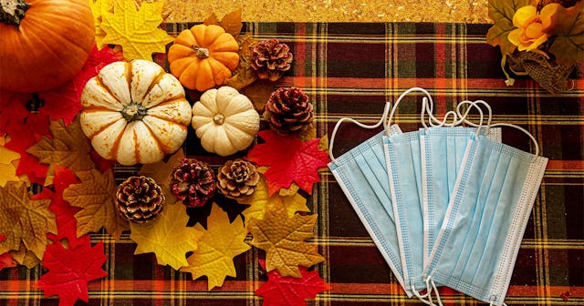 Pumpkins and autumn-colored leaves on a flanneled tablecloth next to medical face masks.