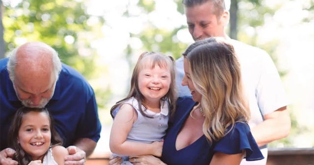 Girl with Down syndrome posing for a family photo with her parents, sister and grandfather
