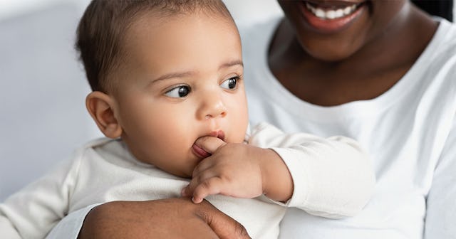 A mother holding her baby who has her hand in her mouth due to the teething stage