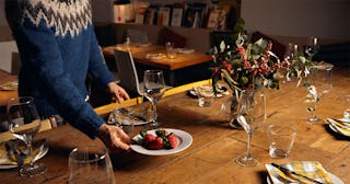 Man setting up the dining table for Thanksgiving dinner, including a centerpiece, plates, cutlery, n...