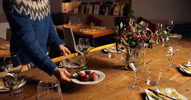 Man setting up the dining table for Thanksgiving dinner, including a centerpiece, plates, cutlery, n...