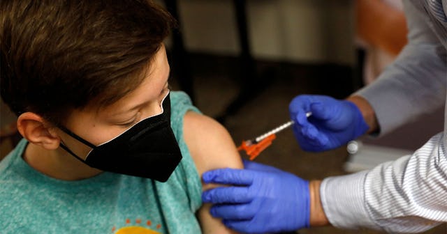 A young boy getting a COVID-19 vaccine while wearing a black medical mask on his face