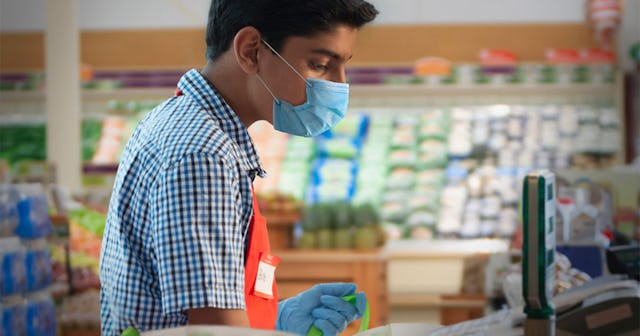 A teen cashier wearing a mask while working in the supermarket