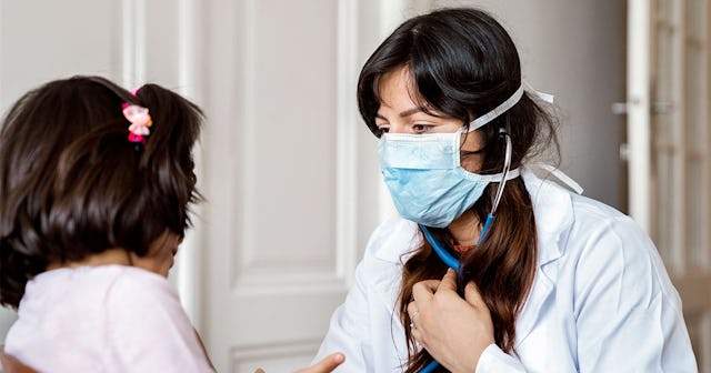 Female doctor wearing a white coat and a blue mask checking her patients hearbeat