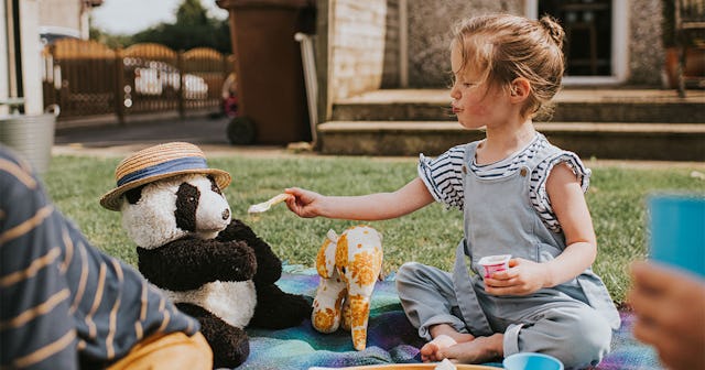 Little girl sitting in a backyard surrounded by plushies feeding her panda toy learning how to share
