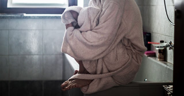 A mentally ill woman sitting alone on her bathtub in a beige bathrobe