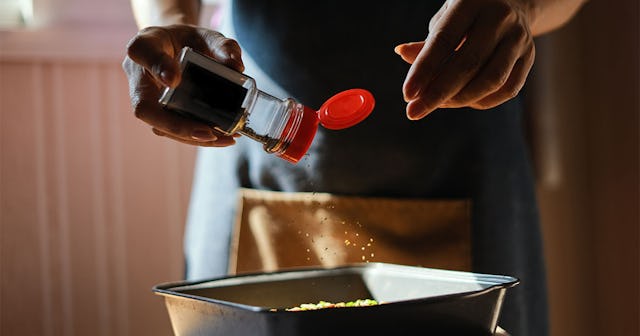 A woman using a small spice bottle to cook