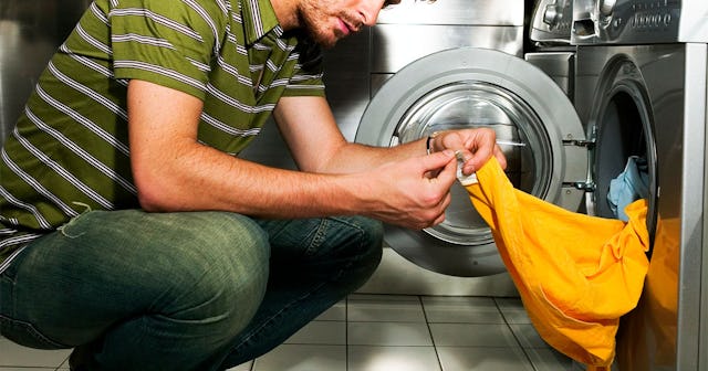 A man in a green and white striped shirt and jeans taking out laundry from the washing machine