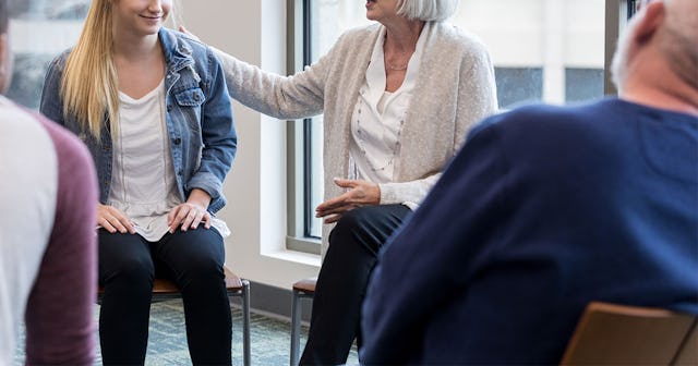 Four people sit in a circle while an older woman holds a girl by her shoulder during recovery high s...