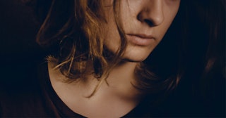 The mid part of a brunette woman's face in a black shirt with a dark background