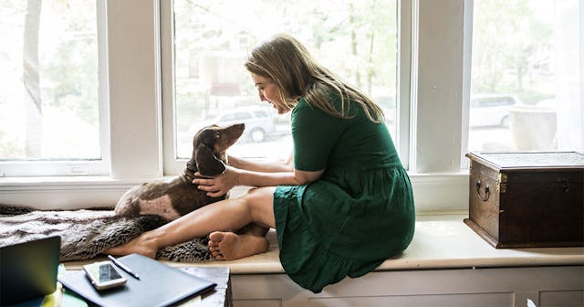 A young blonde woman without kids wearing a green dress and petting her brown dog while sitting in h...