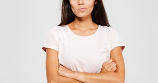 A brunette woman in a white T-shirt with her arms crossed who has sensory sensitivities