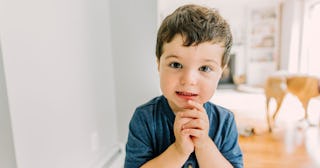 A young boy, with his hands clasped together, saying 'please' to his parents.