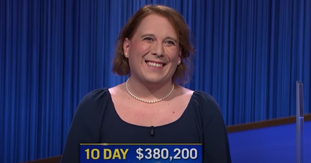 Contestant of the show Jeopardy Amy Schneider wearing a blue dress and smiling with text under her
