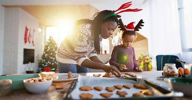 A woman in a Christmas sweater and her daughter, both wearing antler head accessories baking cookies...