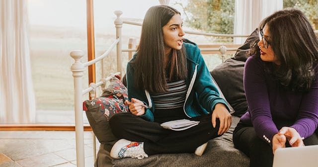 A brown-haired teenage girl sitting on the bed and having an argument with her mother