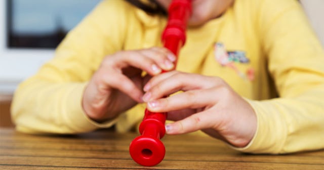 Closeup 3rd-grade student playing red flute, which is considered a torture device while wearing a ye...