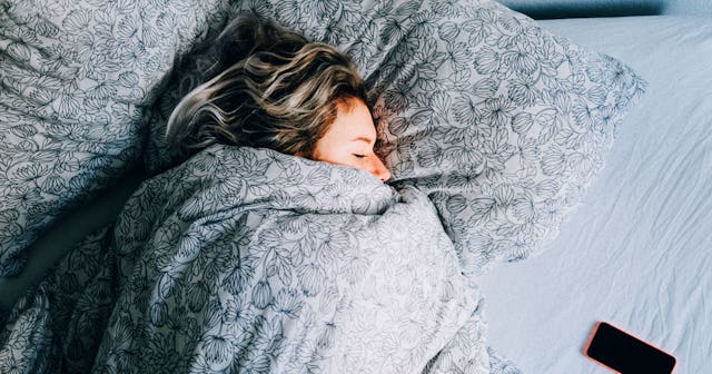 A woman sleeping all tucked in on her side in a bed with grey bed sheets